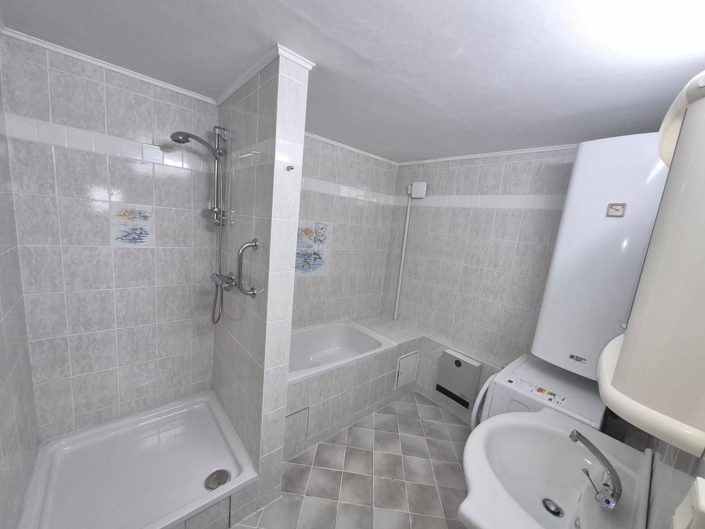 Kleines Badezimmer im Untergeschoss mit Dusche, Badewanne und Waschmaschinenanschluss.