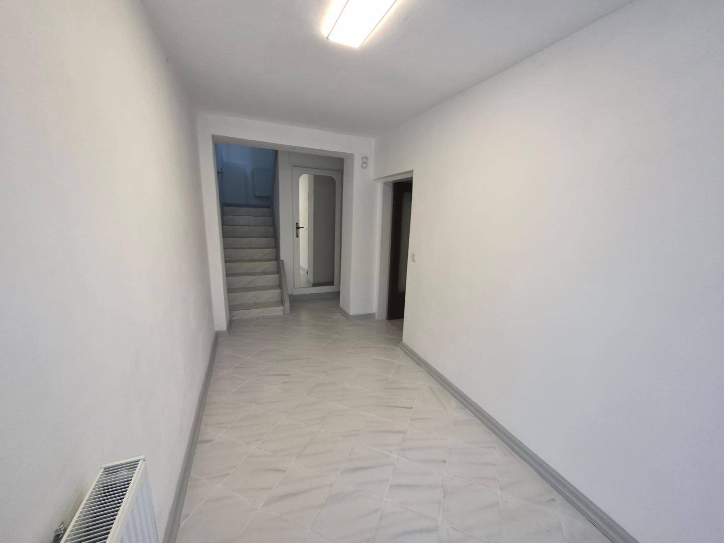 Heller Flur mit Fliesenboden, weiß gestrichenen Wänden und Zugang zu einer Treppe und weiteren Räumen.
