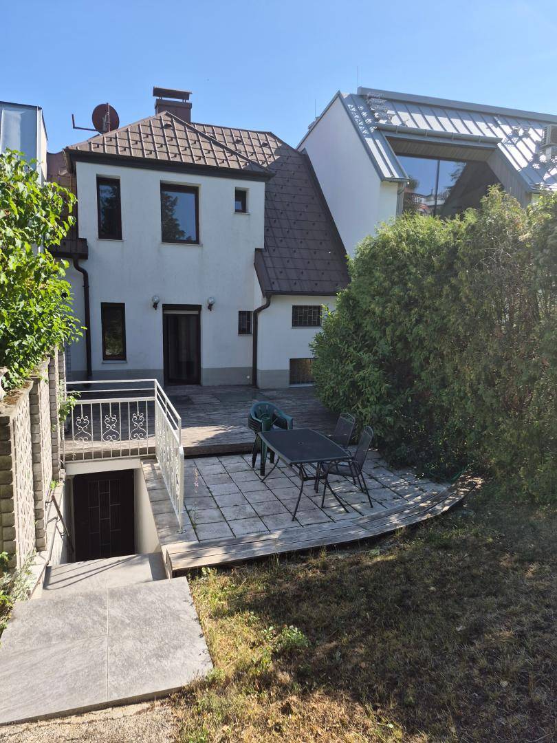Rückseite des Hauses mit großer Holzterrasse, Gartenmöbeln und Zugang zum Gartenbereich.