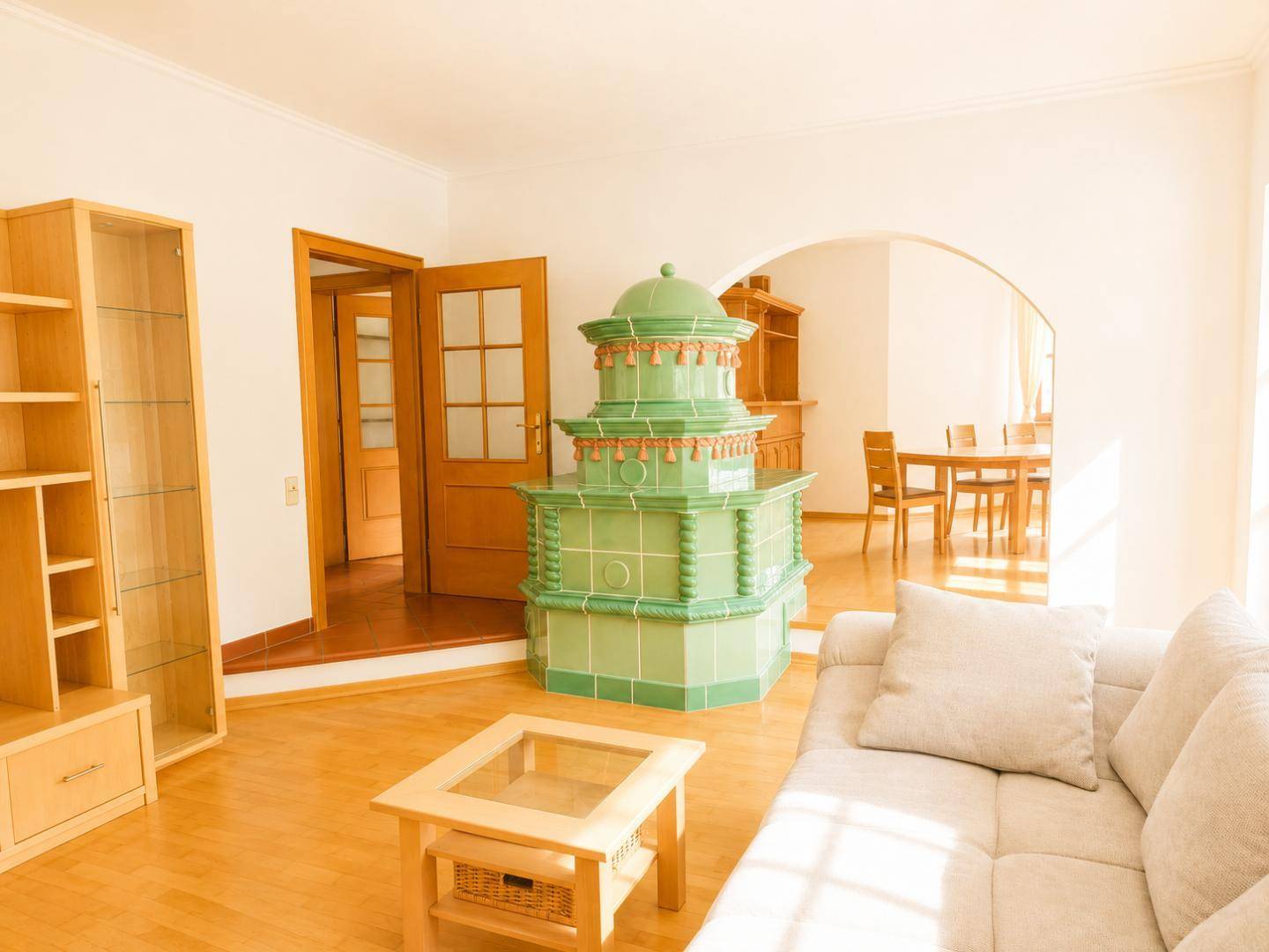 Gemütlicher Wohnbereich mit traditionellem Kachelofen, Sofa und Essbereich im Hintergrund.