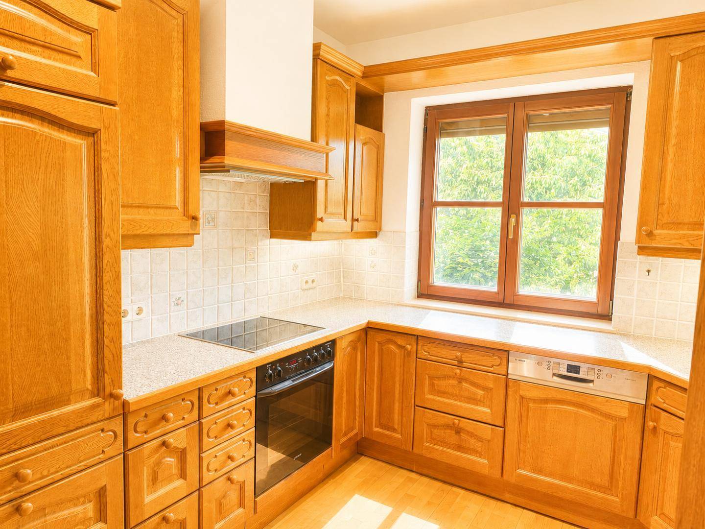 Traditionelle Holzküche mit Einbaugeräten, Fliesenrückwand und einem Fenster über der Spüle.