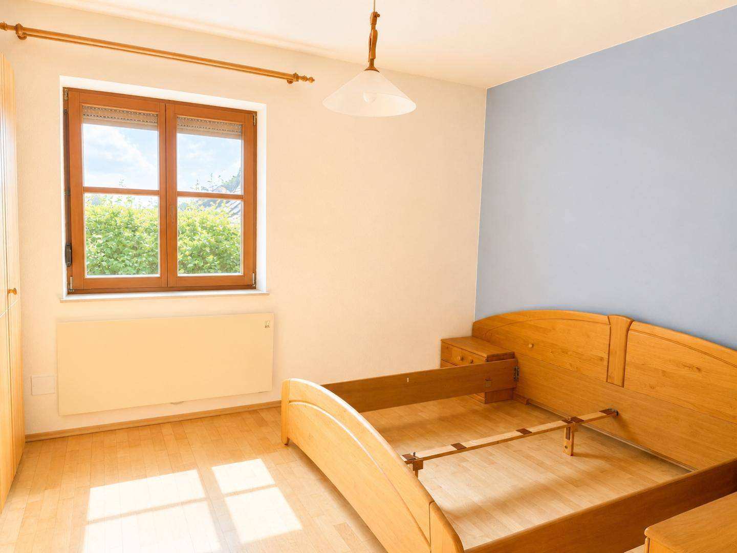 Schlafzimmer mit Holzbettgestell, blauer Akzentwand und Laminatboden, hell und freundlich.