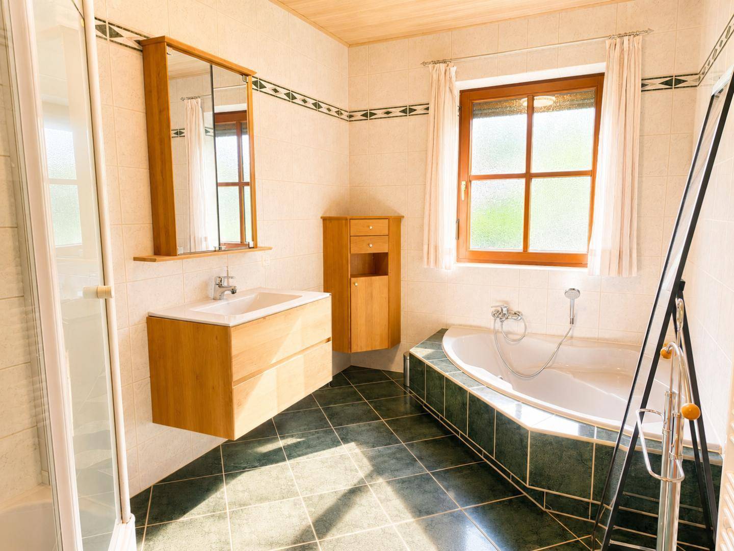 Geräumiges Badezimmer mit Eckbadewanne, Duschkabine, Holzdecke und Fenster für Tageslicht.