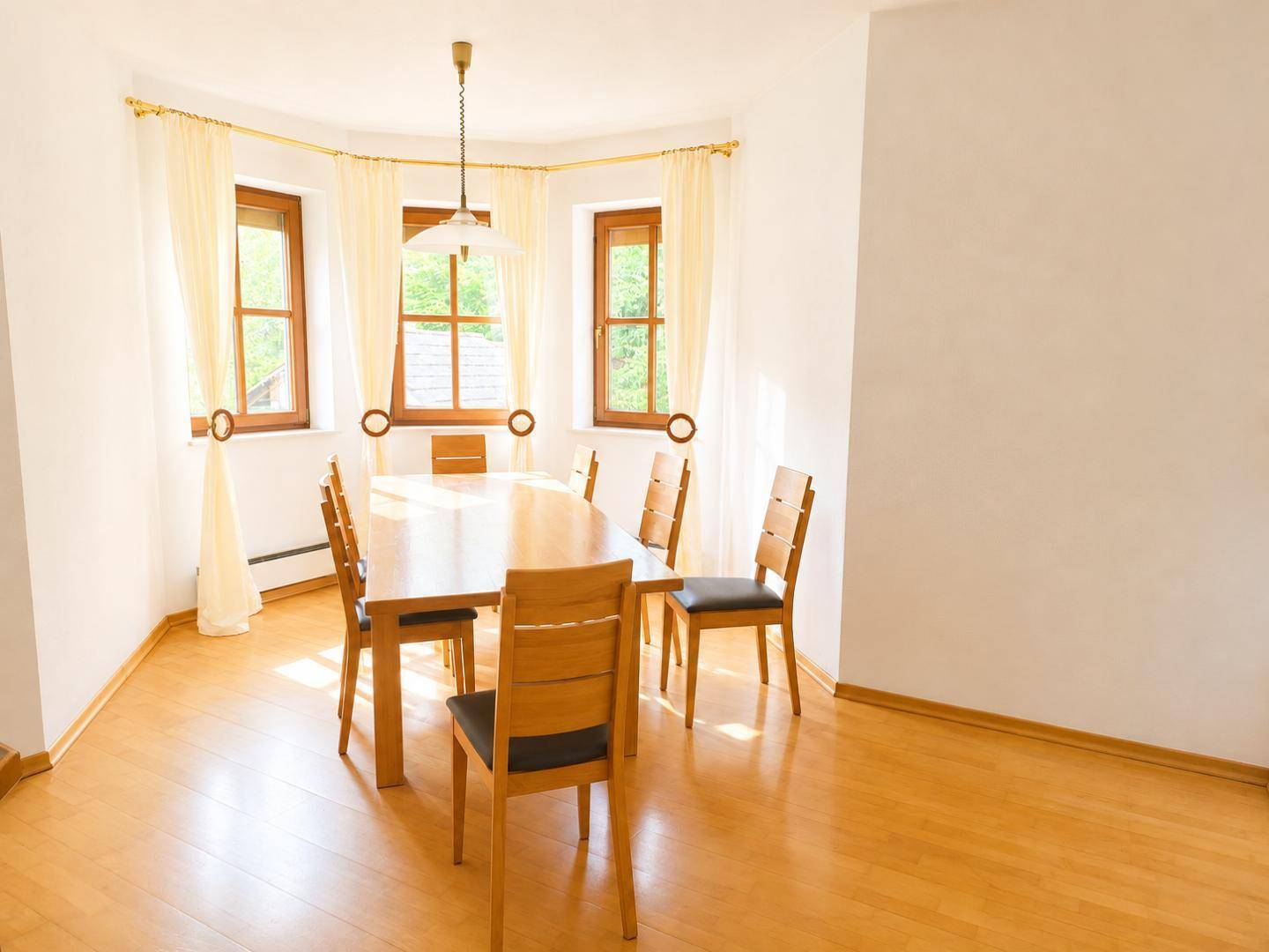 Heller Essbereich mit Holztisch, Stühlen und großen Fenstern, die viel Tageslicht hereinlassen.