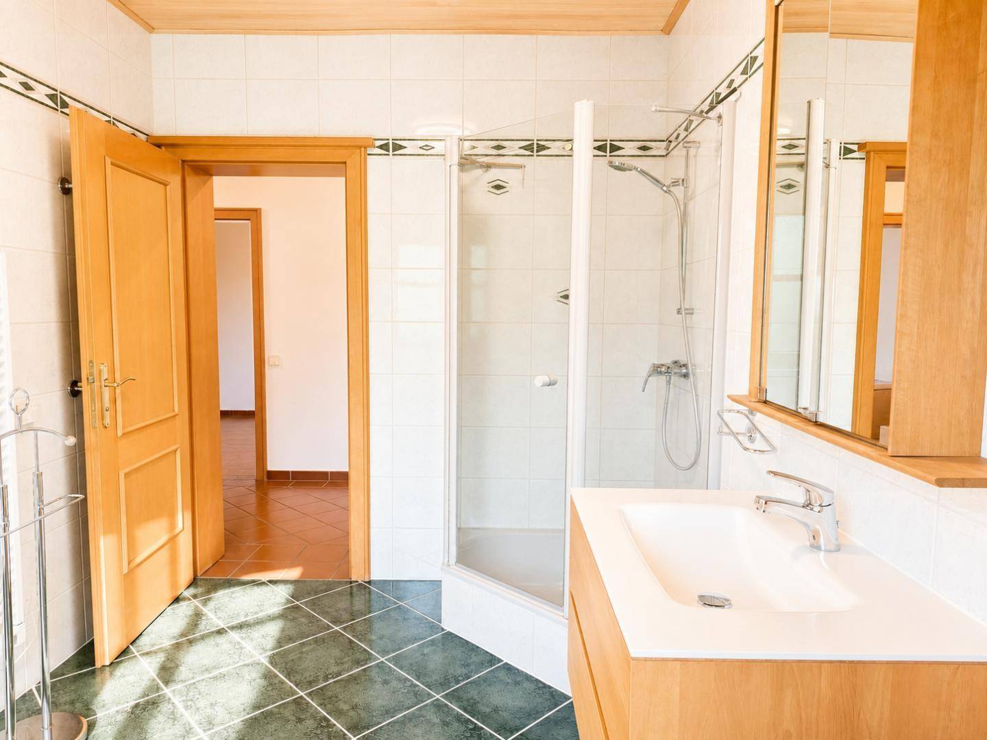 Helles Badezimmer mit Duschkabine, Einzelwaschbecken und dunklen Bodenfliesen in gutem Zustand.