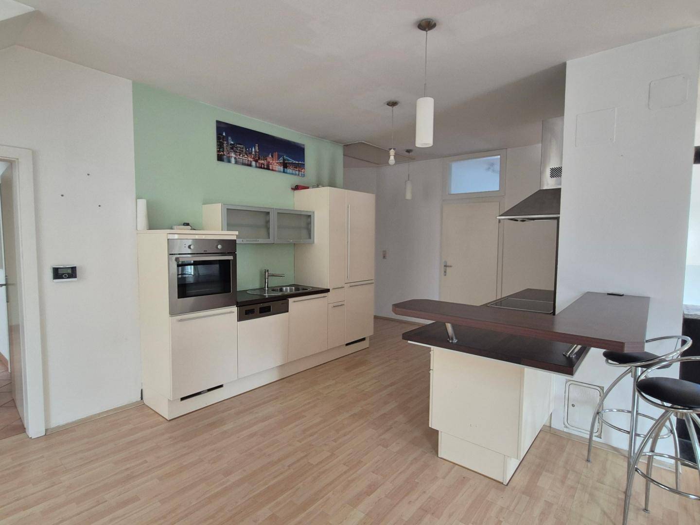 Kompakte Einbauküche mit hellen Schränken, integriertem Backofen und Frühstücksbar.