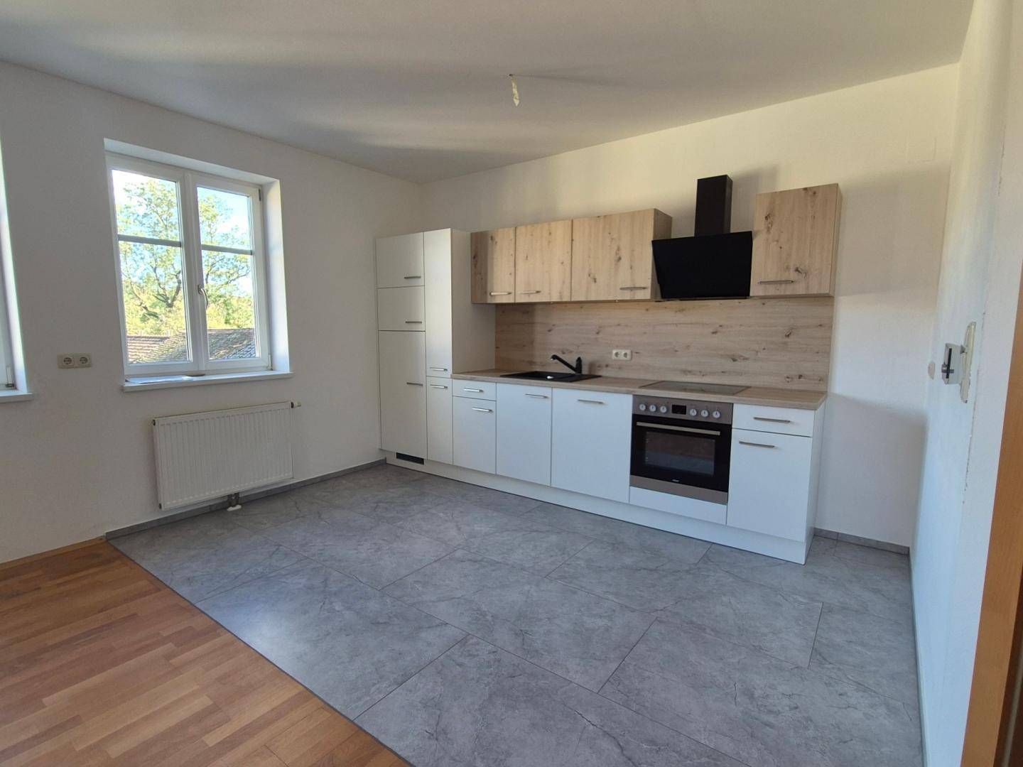 Moderne Küche mit hellen Holzfronten, weißen Unterschränken und grauem Fliesenboden.