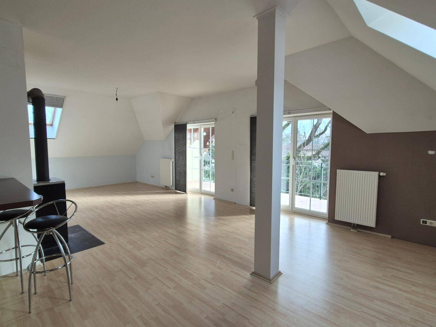 Geräumiges Wohnzimmer im Dachgeschoss mit Holzboden, Kaminofen und Zugang zum Balkon.