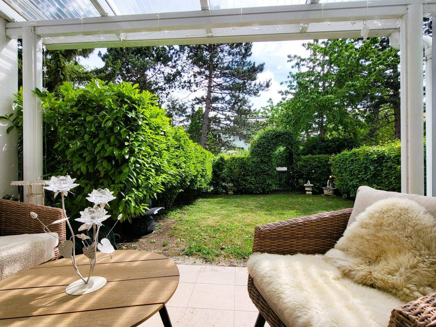 Überdachte Terrasse mit Blick auf den grünen Garten und die umliegende Hecke.