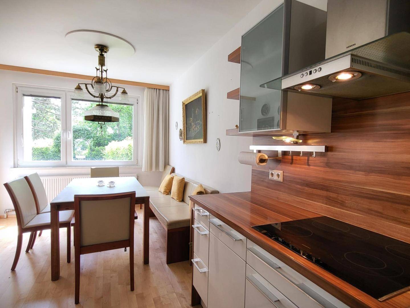 Helle Küche mit Holzarbeitsplatte, integriertem Kochfeld und Essbereich am Fenster.