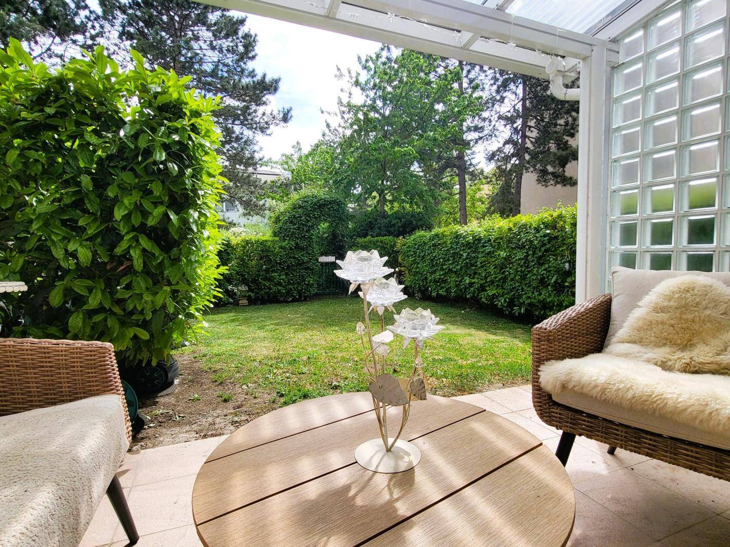 Gemütliche Terrasse mit Rattanmöbeln und einem gepflegten Garten im Hintergrund.