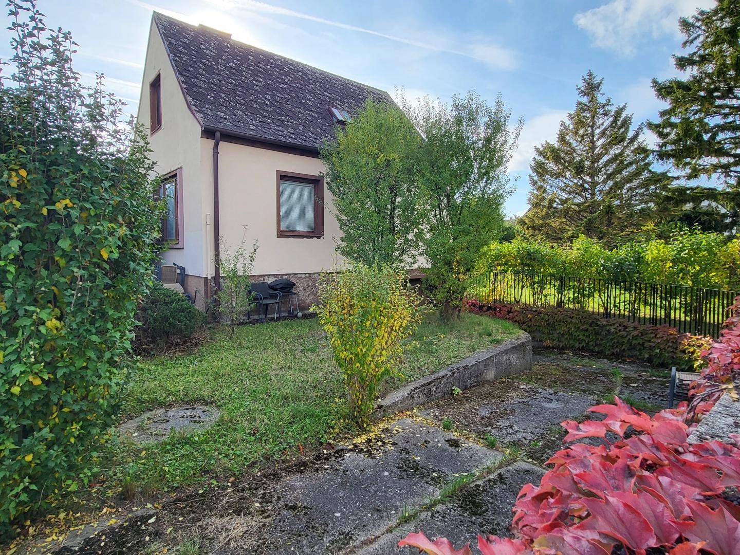 Seitenansicht des Hauses mit einem kleinen Gartenbereich und herbstlicher Bepflanzung im Vordergrund.