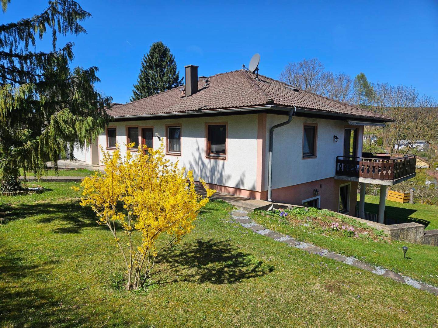 Seitenansicht des Hauses mit kleinem Balkon und blühendem Forsythienbusch im Vorgarten.