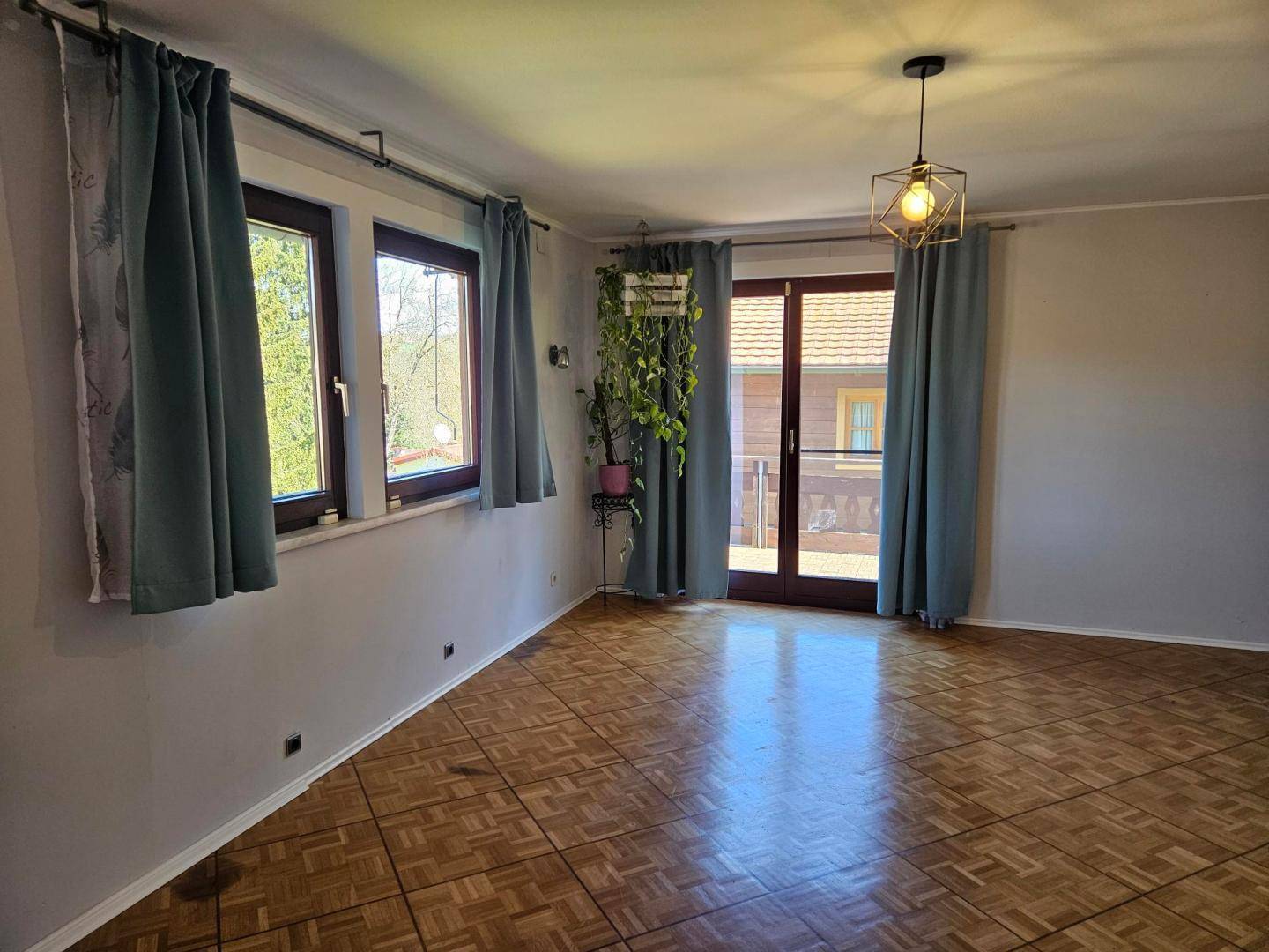 Geräumiges Zimmer mit Parkettboden, großen Fenstern und Zugang zu einem Außenbereich.