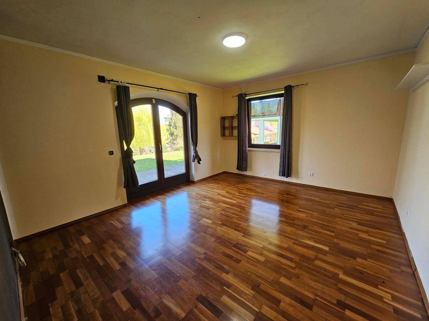 Helles Zimmer mit Parkettboden und direktem Zugang zum Garten durch eine große Tür.