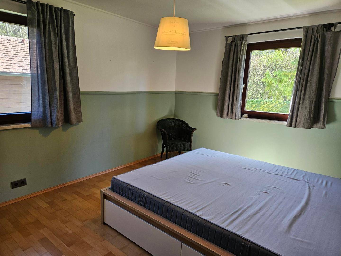 Gemütliches Schlafzimmer mit Parkettboden, zwei Fenstern und einer modernen Bettkonstruktion.