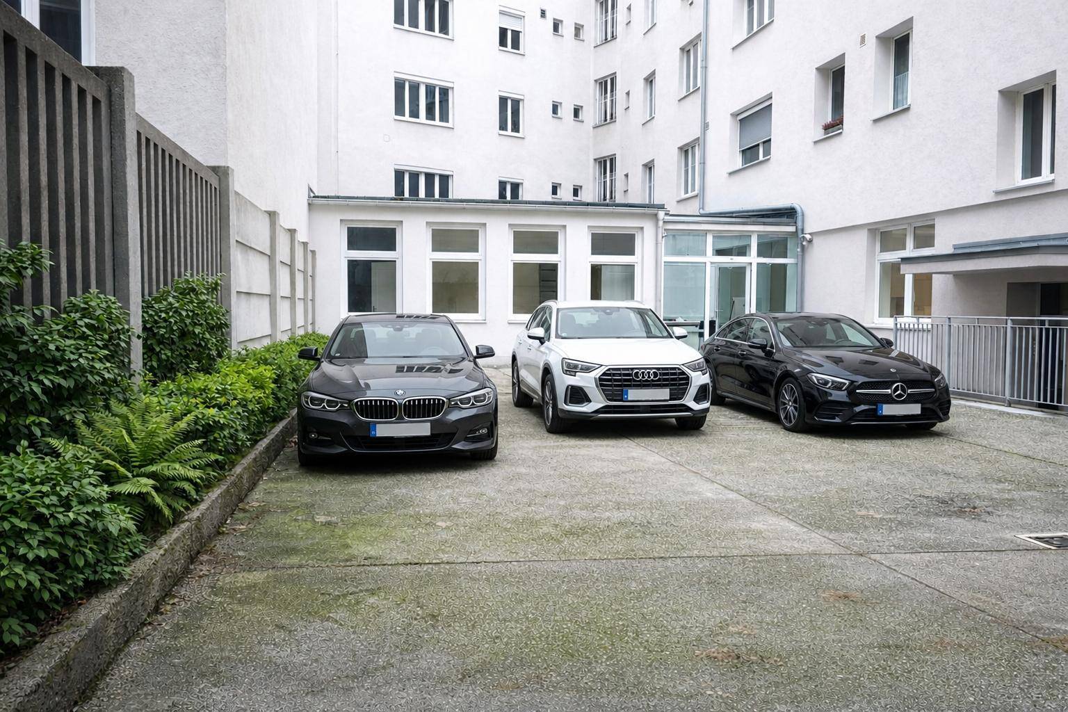 Außenparkplatz mit drei Autos, umgeben von einem Gebäude und etwas Grünfläche im Innenhof.