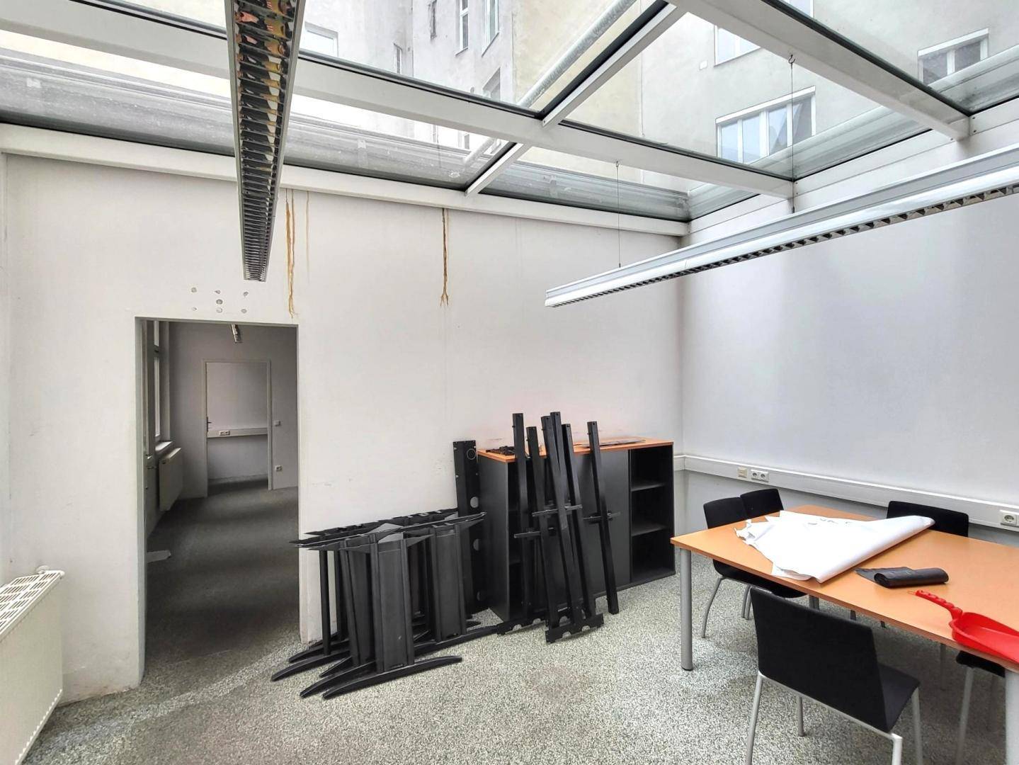 Büroraum mit Glasdach und Oberlichtern, gestapelten Möbeln und einem Arbeitstisch, bietet viel Tageslicht.