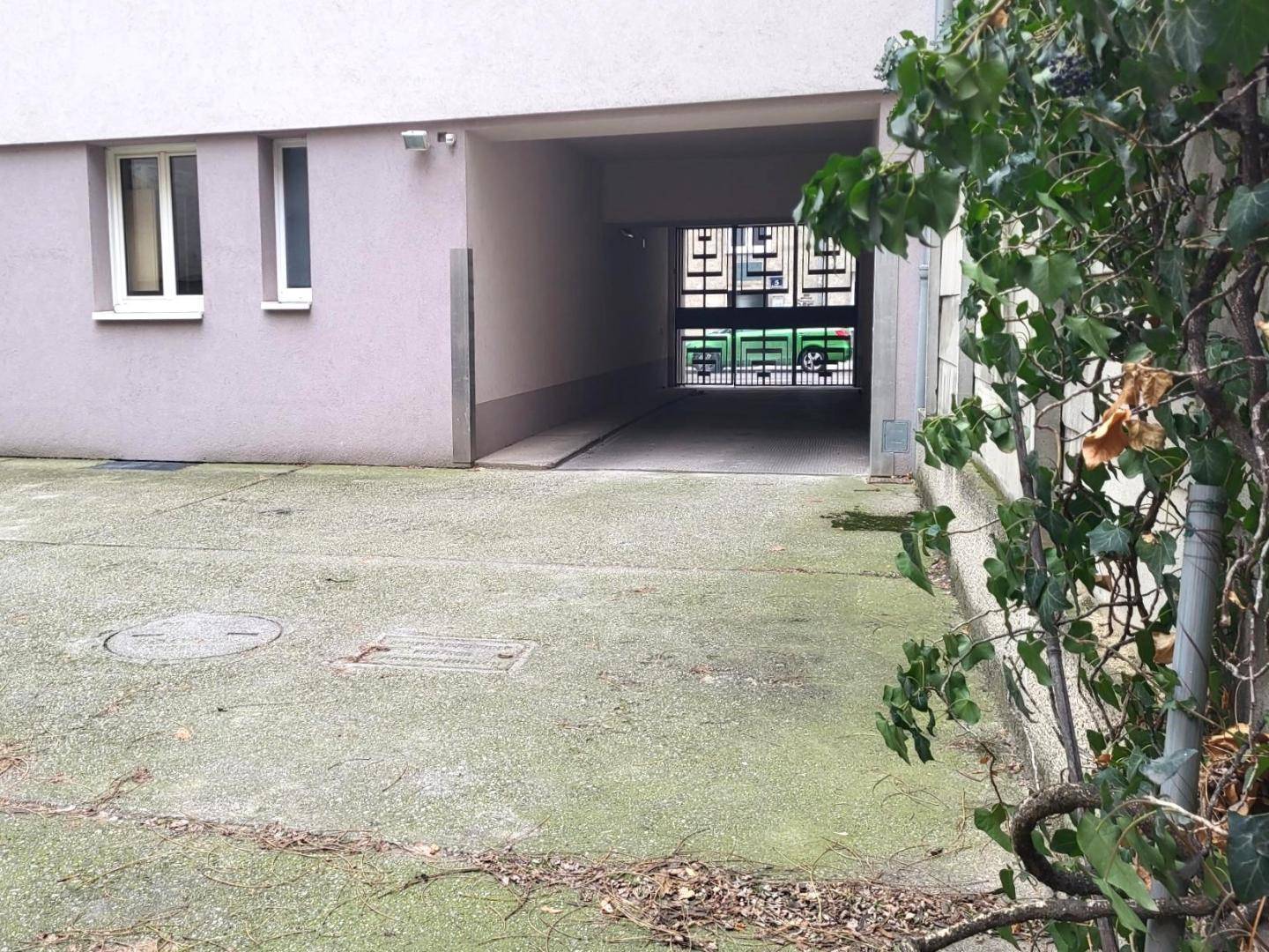 Einfahrt zu einem Parkbereich oder einer Tiefgarage mit Betonboden und etwas Bewuchs an der Seite.