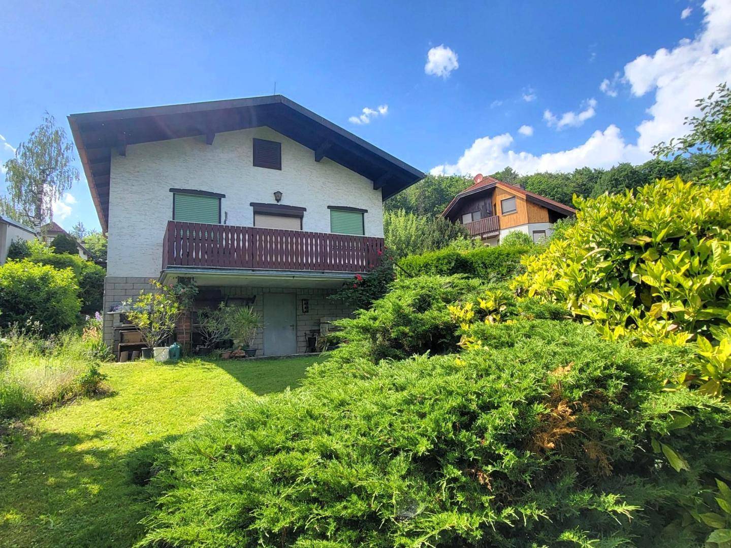 Ansicht des Hauses von der Gartenseite mit Balkon und üppiger Bepflanzung im Vordergrund.