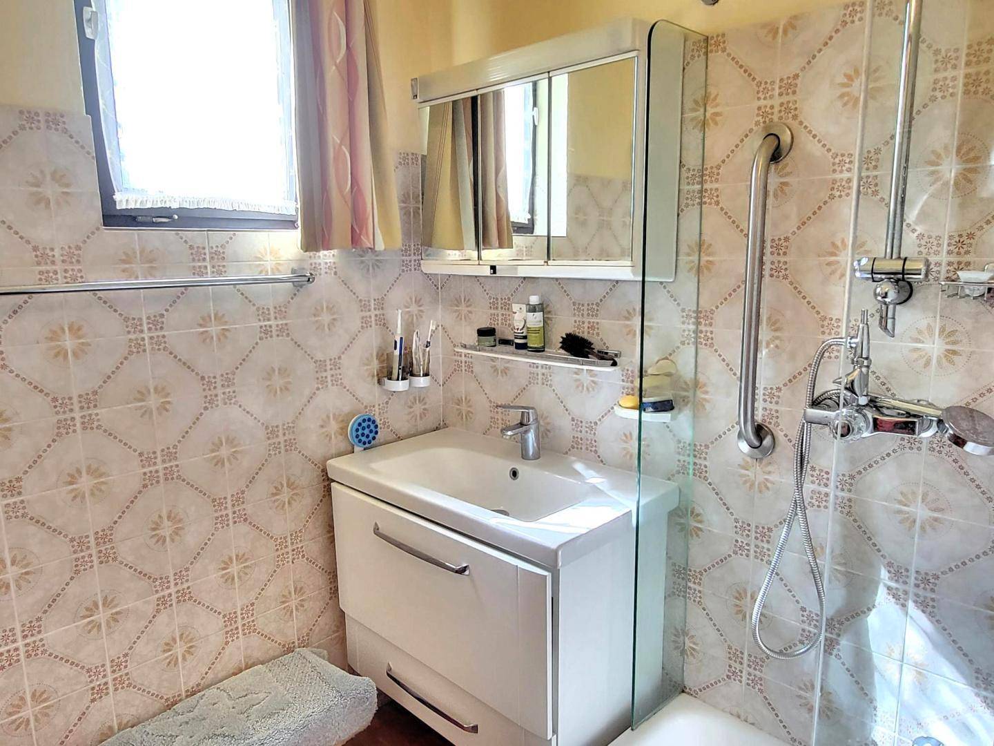Helles Badezimmer mit gemusterten Fliesen, Duschbereich und modernem Waschtisch mit Spiegelschrank.