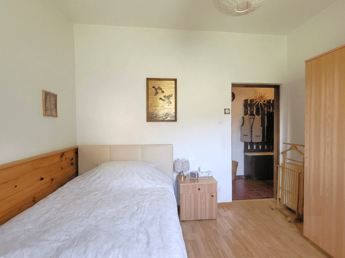 Helles Schlafzimmer mit Einzelbett, Holzvertäfelung und Zugang zum Flur.