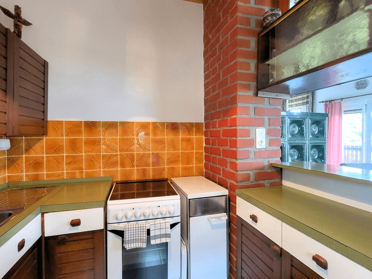 Rustikale Küche mit orangefarbenen Fliesen, Backofen und integriertem Kühlschrank.