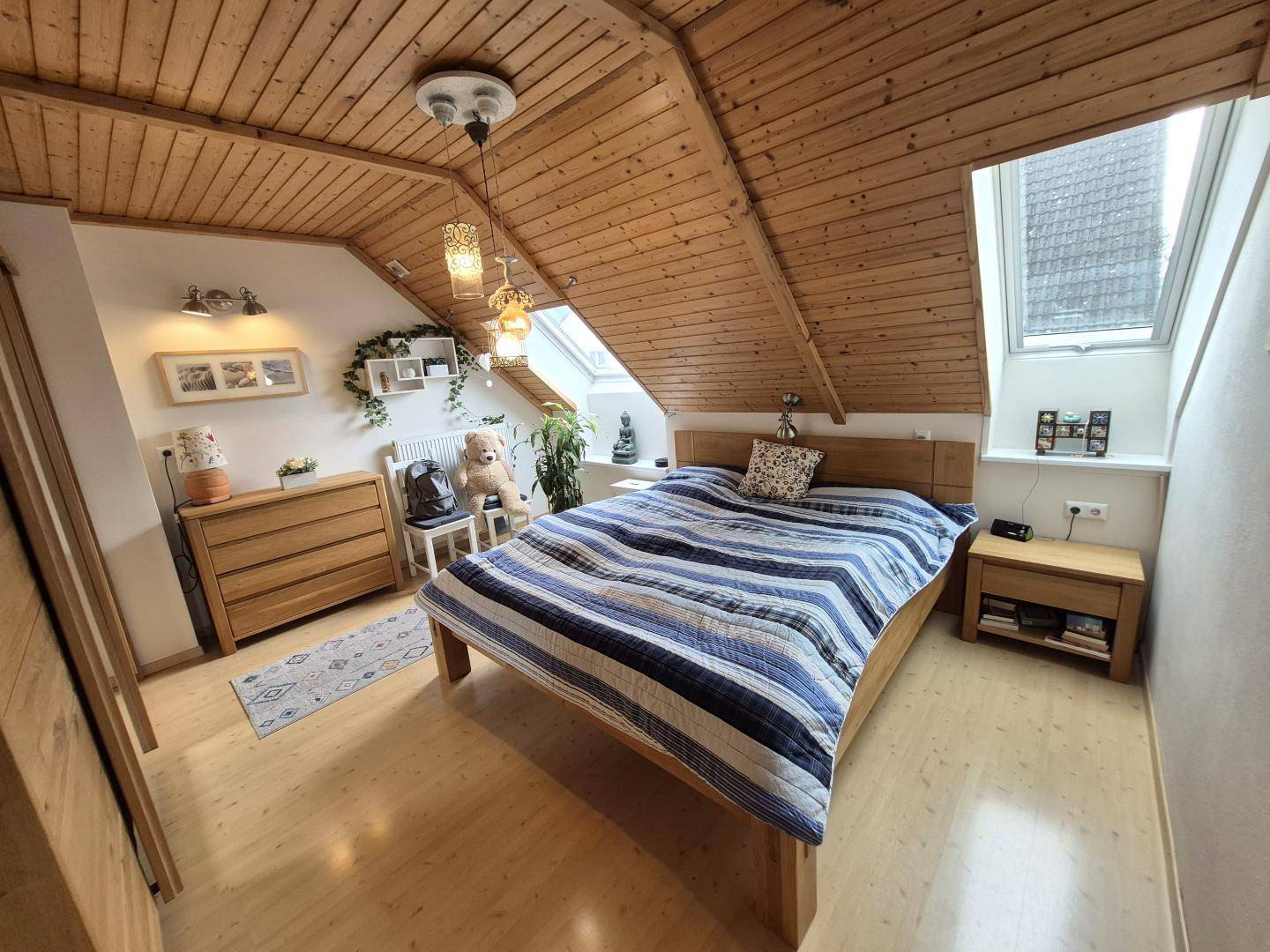 Gemütliches Schlafzimmer im Dachgeschoss mit Holztäfelung, Dachfenster und bequemen Bett.