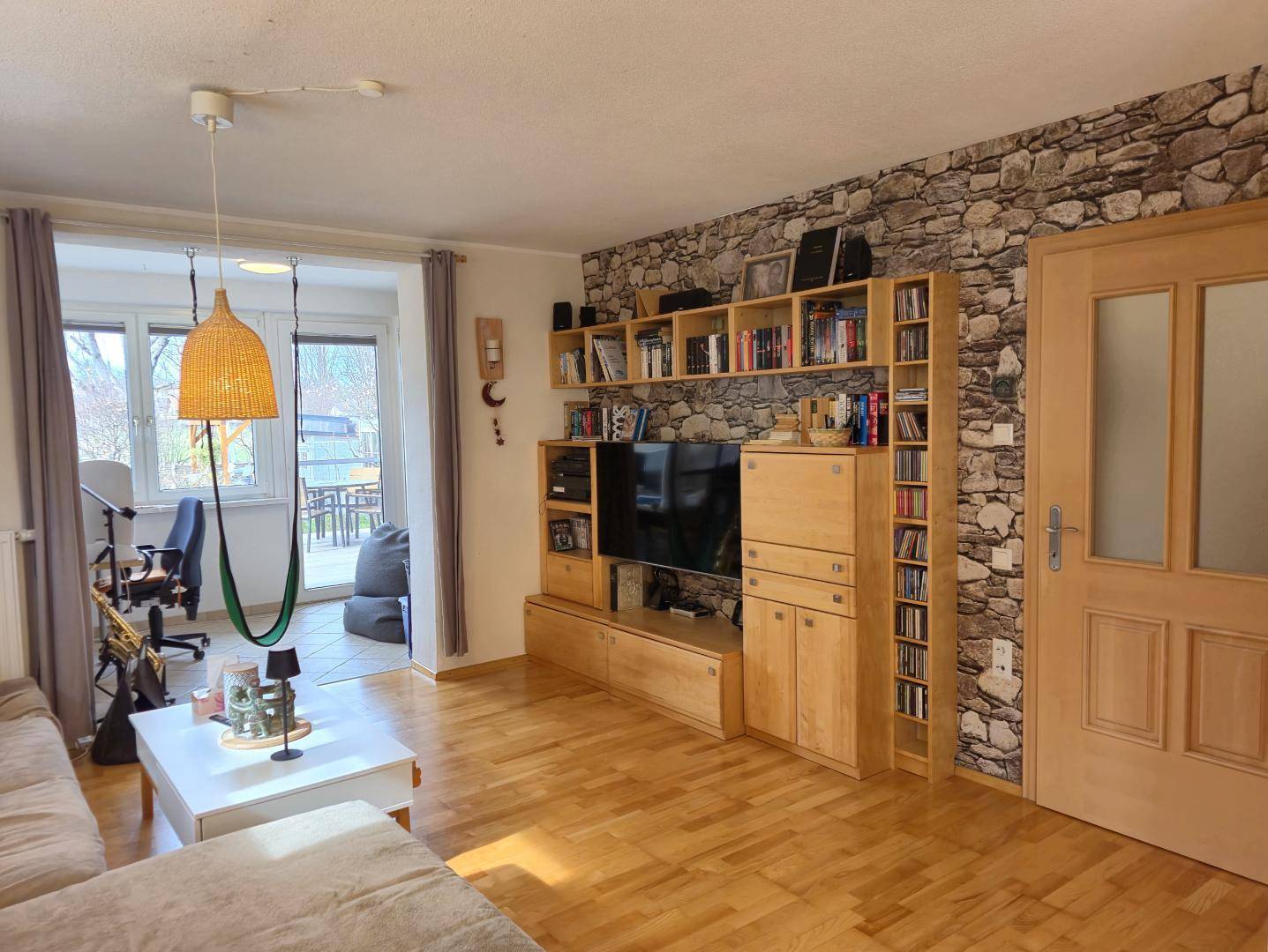 Geräumiges Wohnzimmer mit Holzboden, großer Couch und einer Steinwand-Akzentfläche.