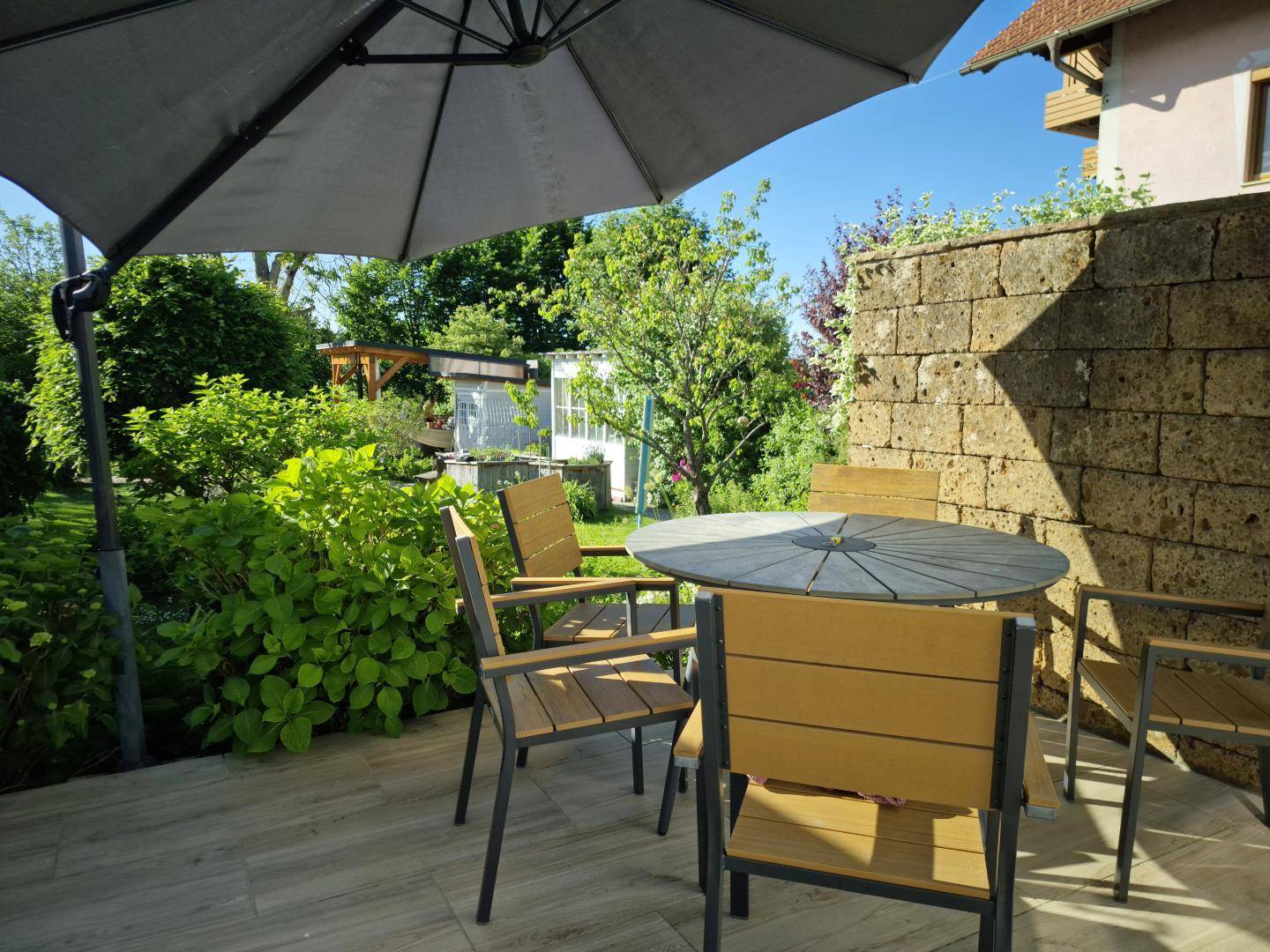 Gemütliche Terrasse mit Steinfliesen, Gartenmöbeln und einem großen Sonnenschirm für entspannte Stunden.