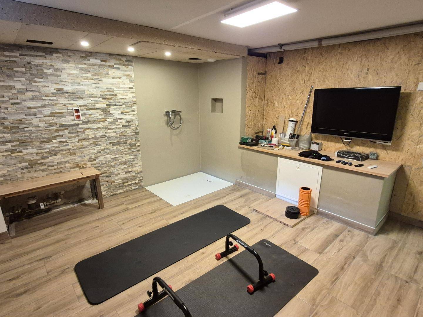 Geräumiger Fitnessraum im Keller mit Trainingsmatten, Fernseher und Steinwand.