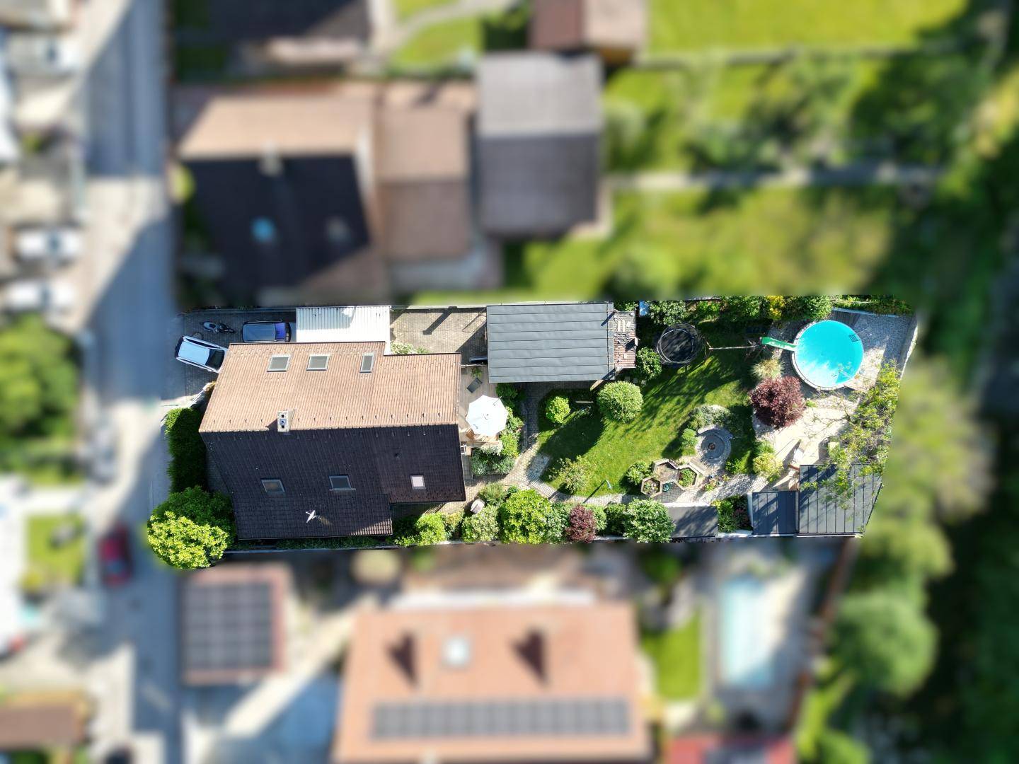 Luftaufnahme des Grundstücks mit Haus, Garten, Pool und umliegender Bebauung.