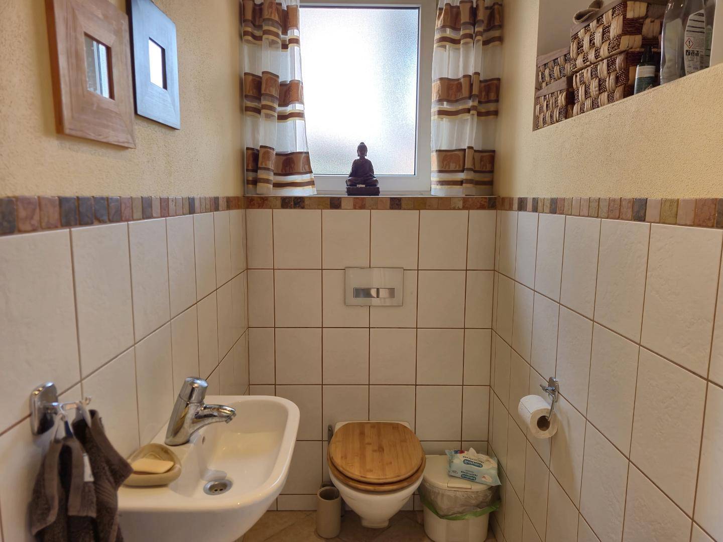 Kleines Gäste-WC mit Fliesen, Waschbecken und Fenster, funktional und hell gestaltet.