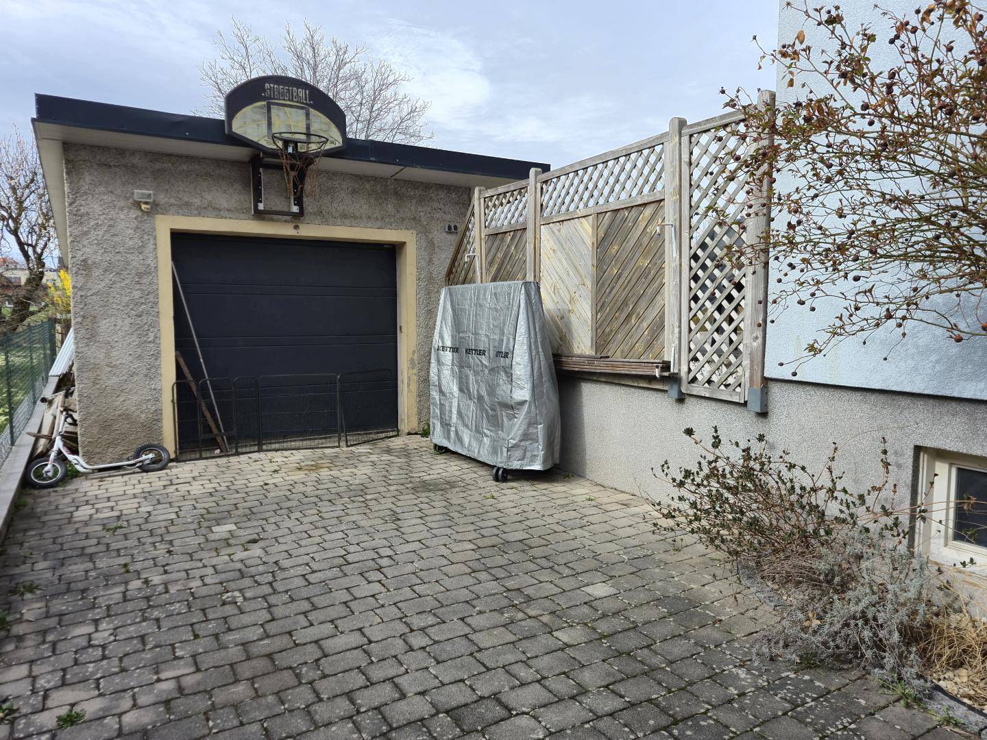 Einzelgarage mit Basketballkorb und gepflasterter Zufahrt.
