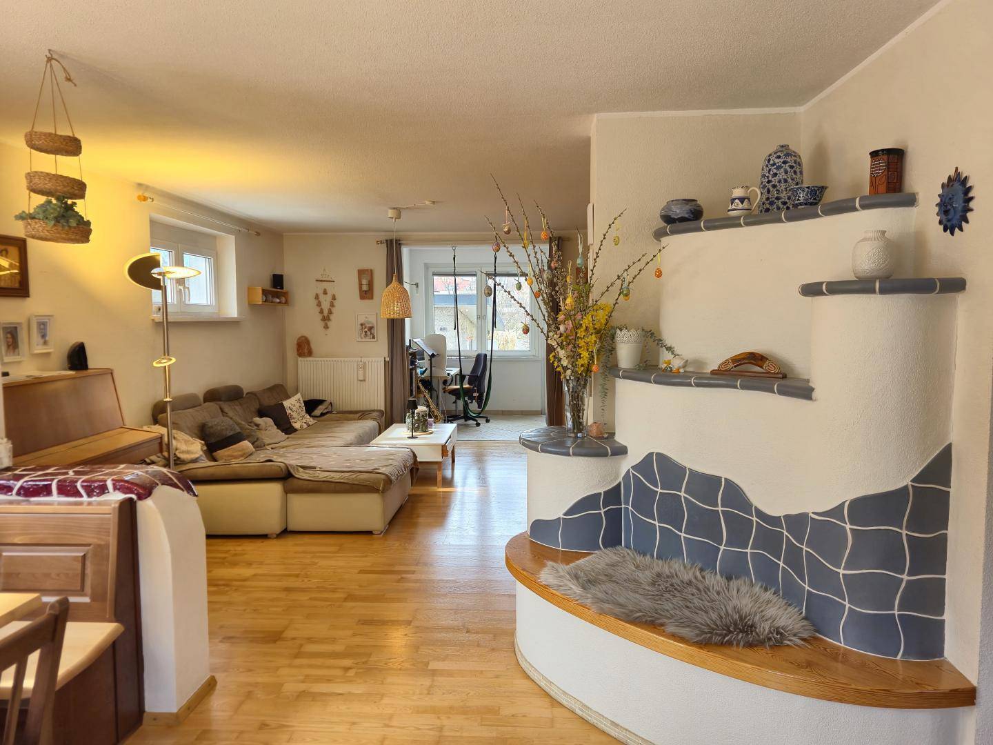 Geräumiges Wohnzimmer mit Holzboden und einem dekorativen Kachelofen mit integrierter Sitzbank.