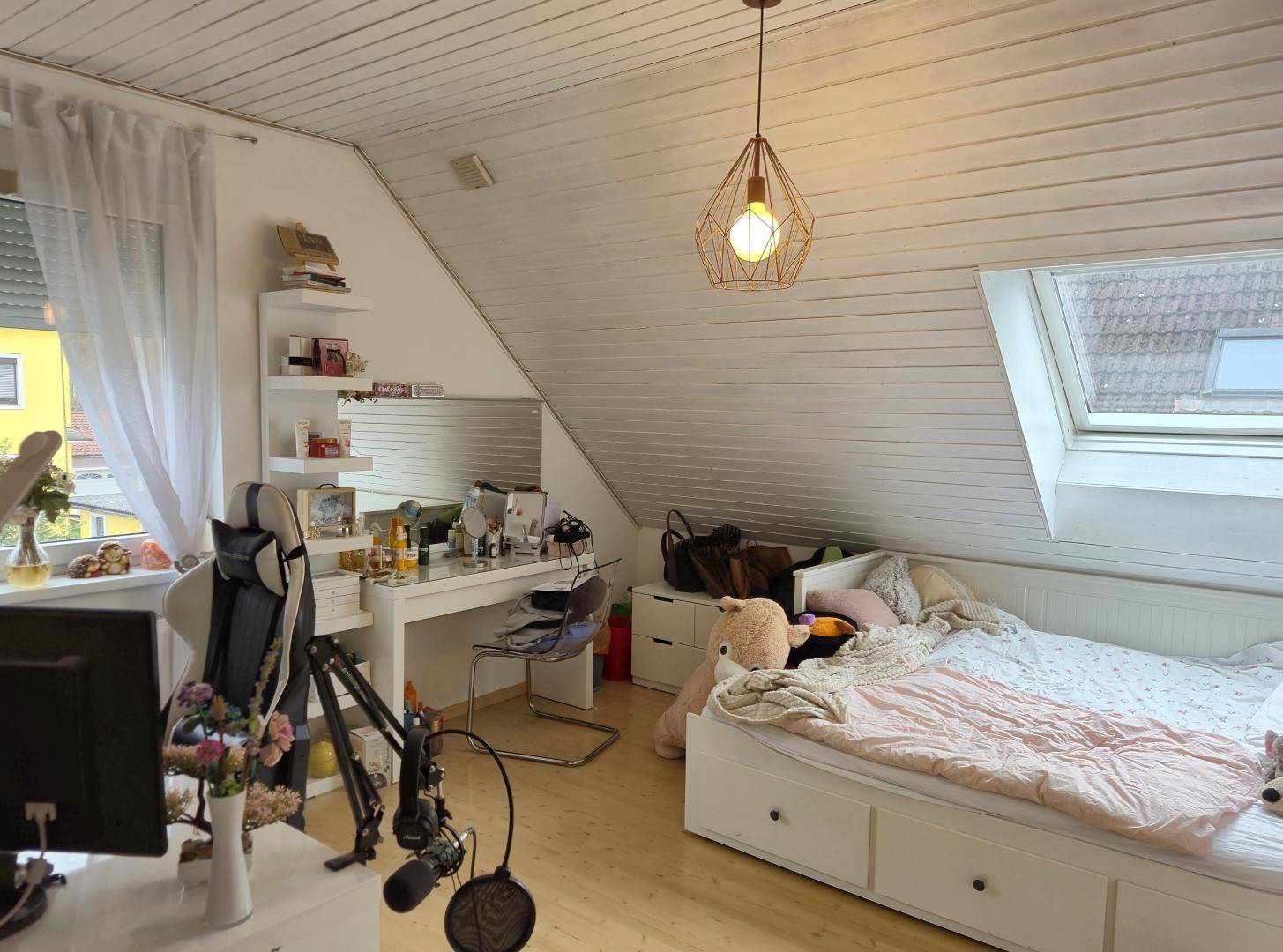 Vielseitiges Zimmer im Dachgeschoss mit Bett, Schminktisch und Dachfenster, hell und funktional.
