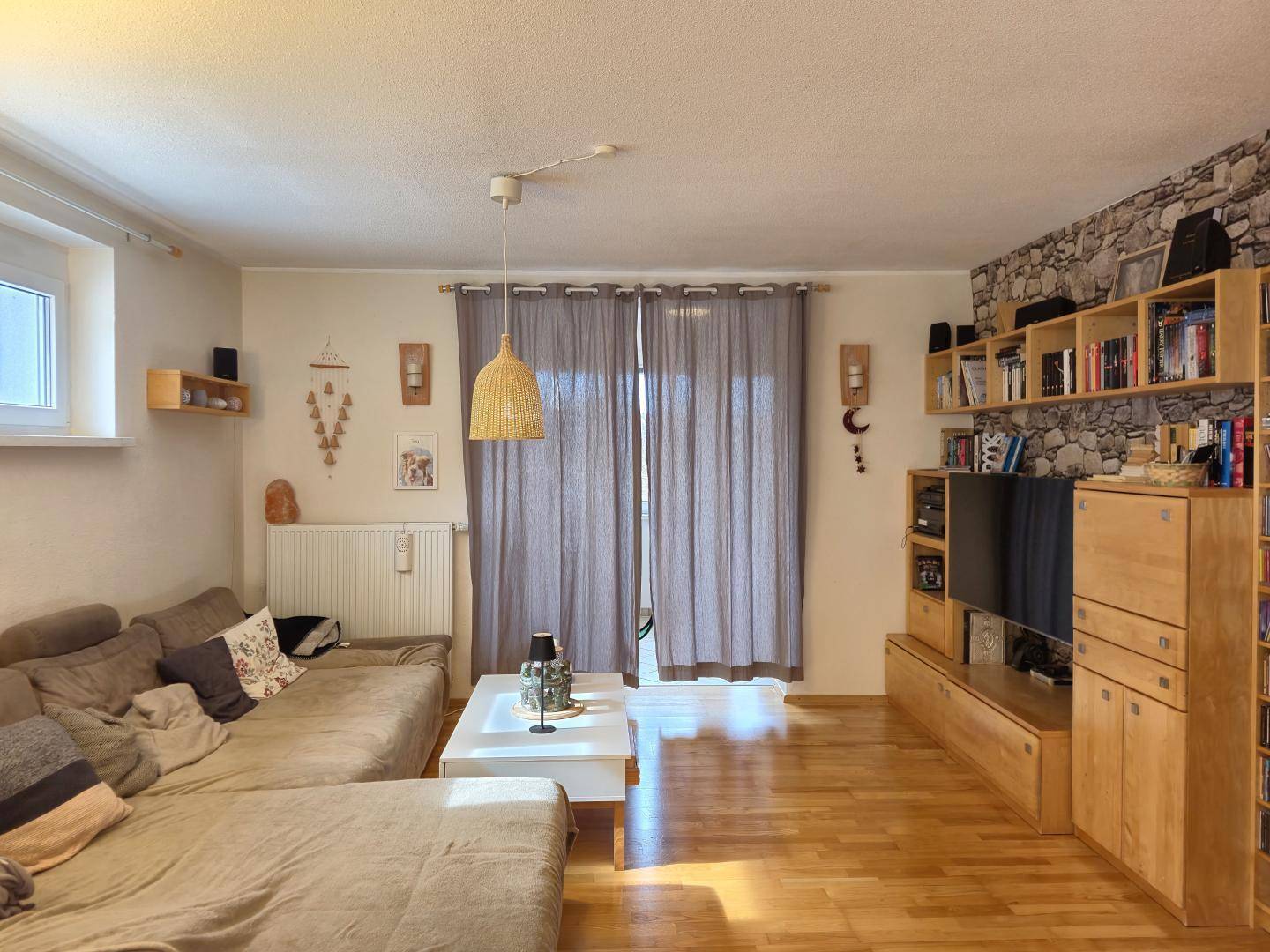 Helles Wohnzimmer mit Holzfußboden, bequemer Eckcouch und einer Wand mit Steinoptik-Tapete.
