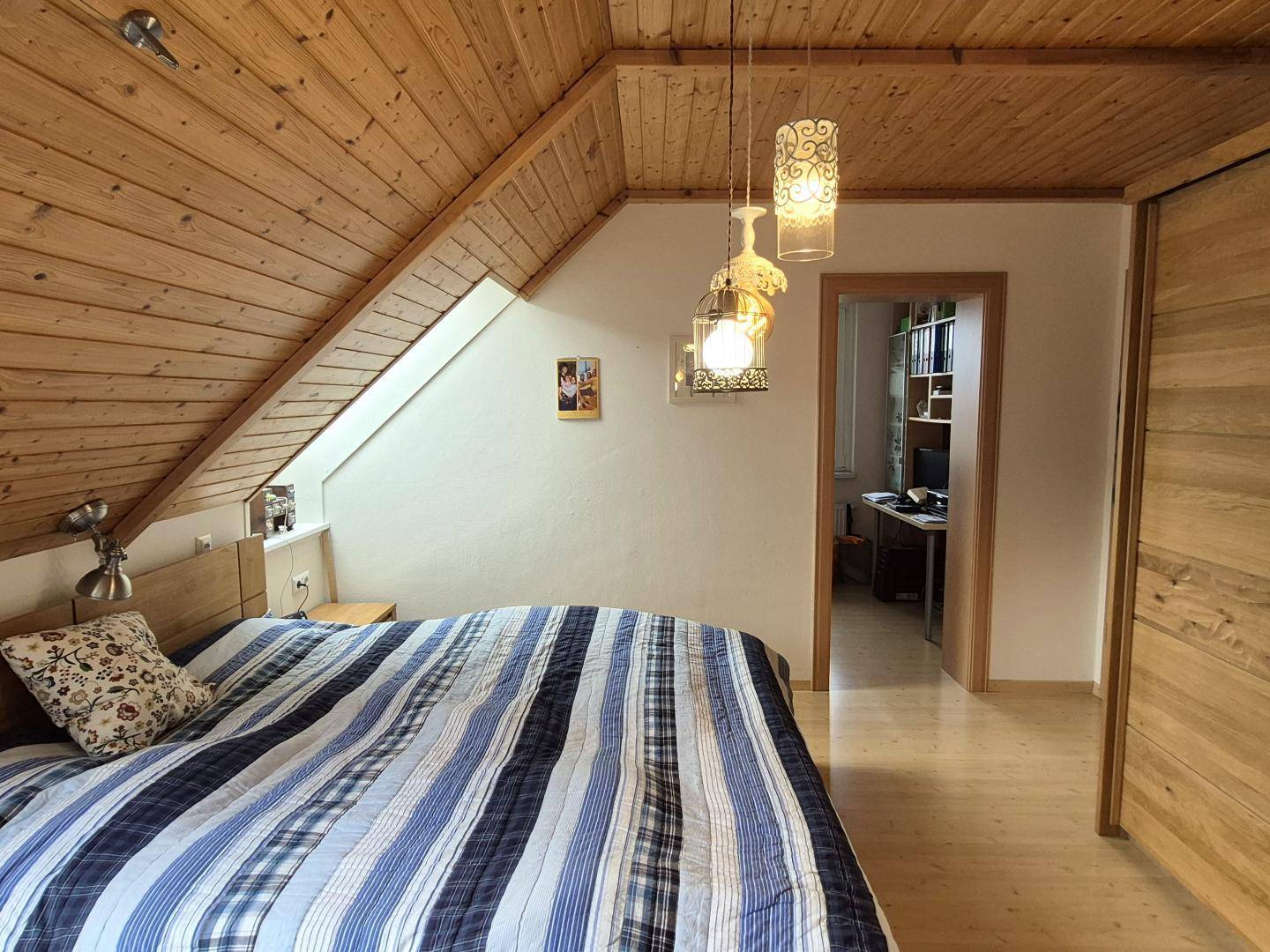 Schlafzimmer mit Holzbalkendecke und Zugang zu einem weiteren Raum im Dachgeschoss.