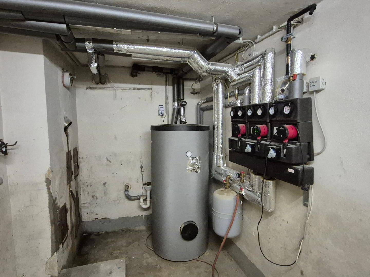 Heizungsraum im Keller mit Warmwasserspeicher und komplexem Rohrsystem.