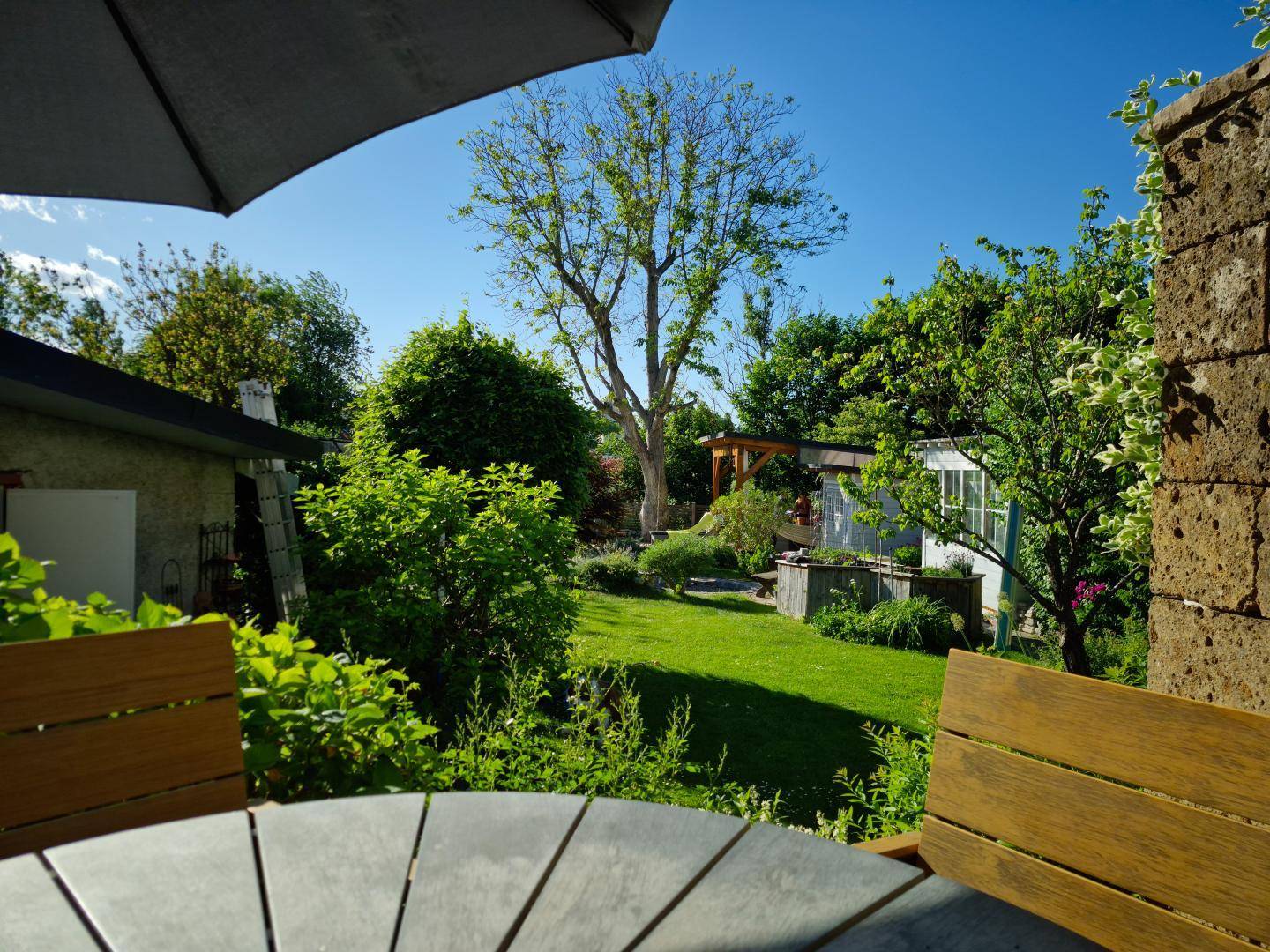 Weitläufiger Gartenbereich mit altem Baumbestand und viel Grün, gesehen von einer erhöhten Terrasse.