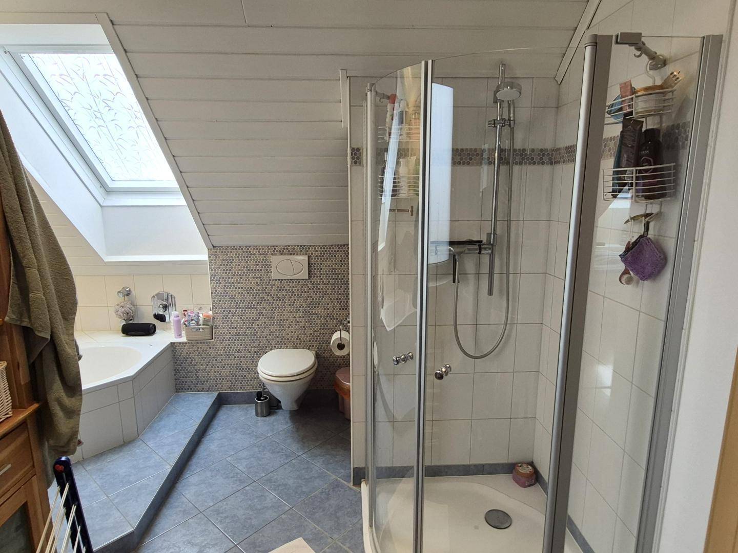 Badezimmer mit Duschkabine, WC und Eckbadewanne unter dem Dachfenster.