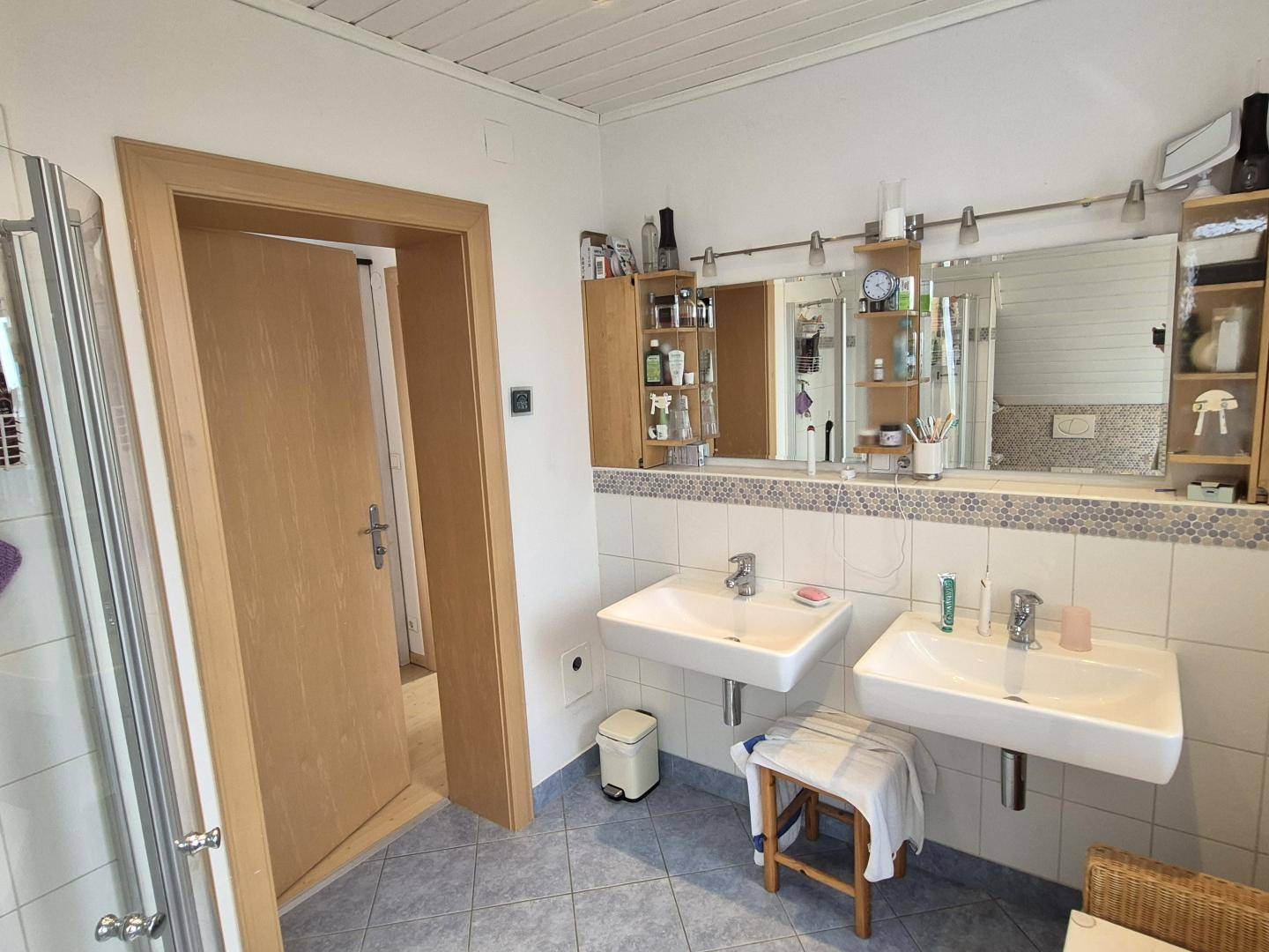 Badezimmer mit Doppelwaschbecken, Spiegelschrank und Zugang zu einem weiteren Raum.