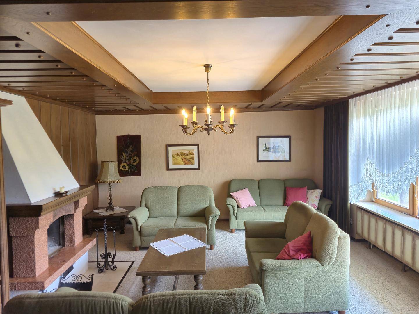 Wohnzimmer mit Kamin, bequemen Sofas und traditioneller Holzvertäfelung an Decke und Wänden.