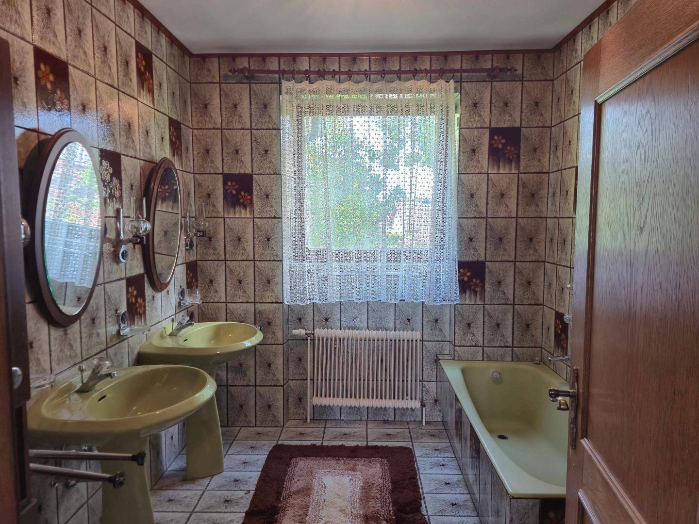 Badezimmer im 80er-Jahre-Stil mit gelben Waschbecken, Badewanne und gemusterten Fliesen.
