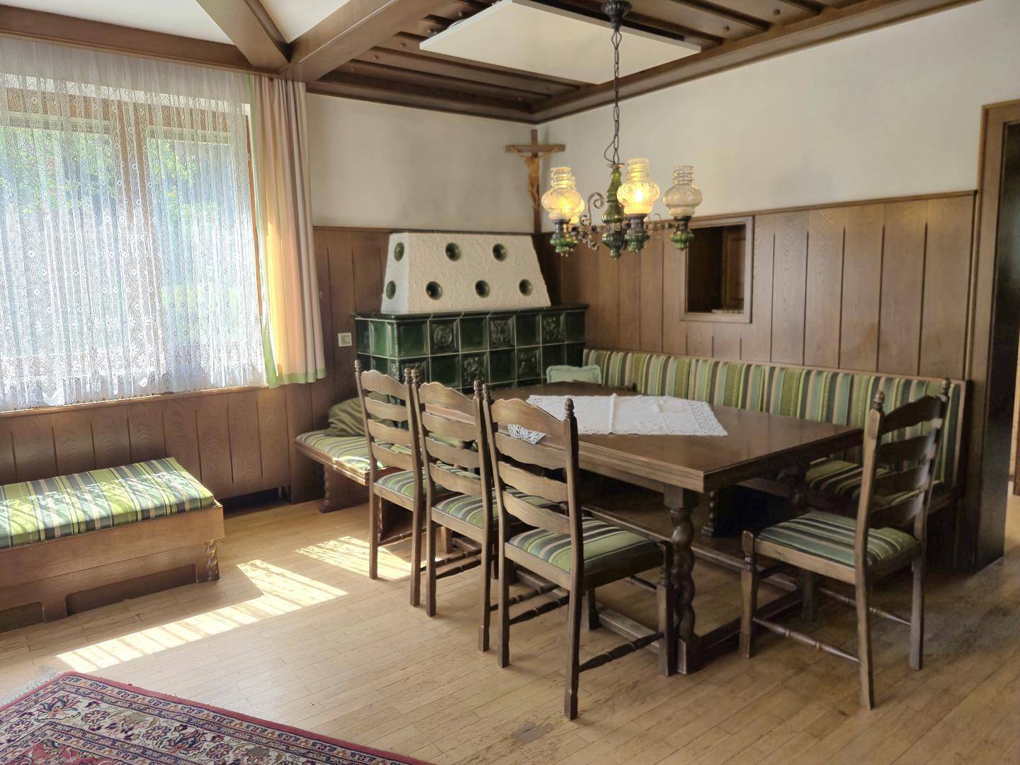 Traditioneller Essbereich mit Kachelofen, Holztisch und gepolsterten Sitzbänken.