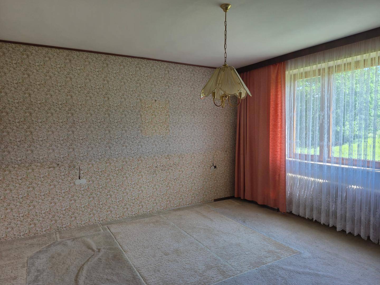 Leeres Zimmer mit gemusterter Tapete, Teppichboden und großem Fenster.