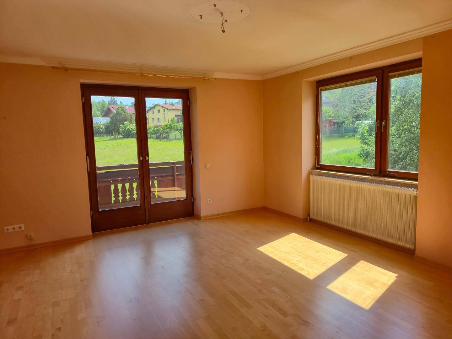 Helles Zimmer mit Holzboden und Zugang zu einem Balkon, bietet einen weiten Blick ins Grüne.