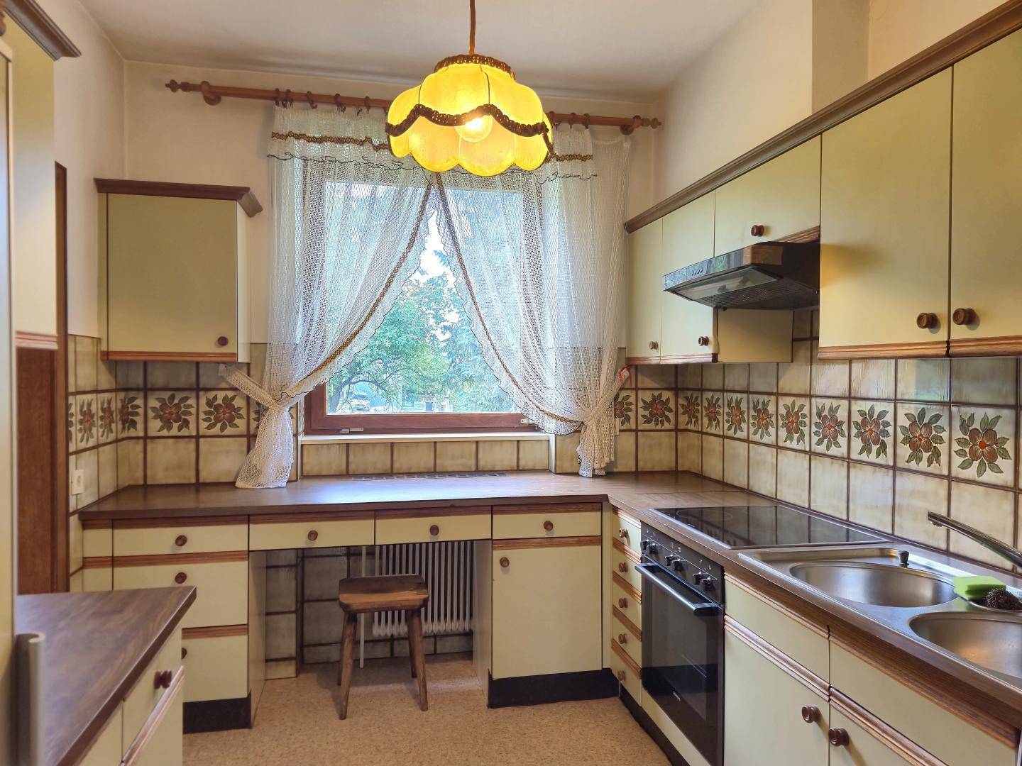 Küche im 80er-Jahre-Stil mit hellgrünen Schränken, gemusterten Fliesen und Fensterblick.