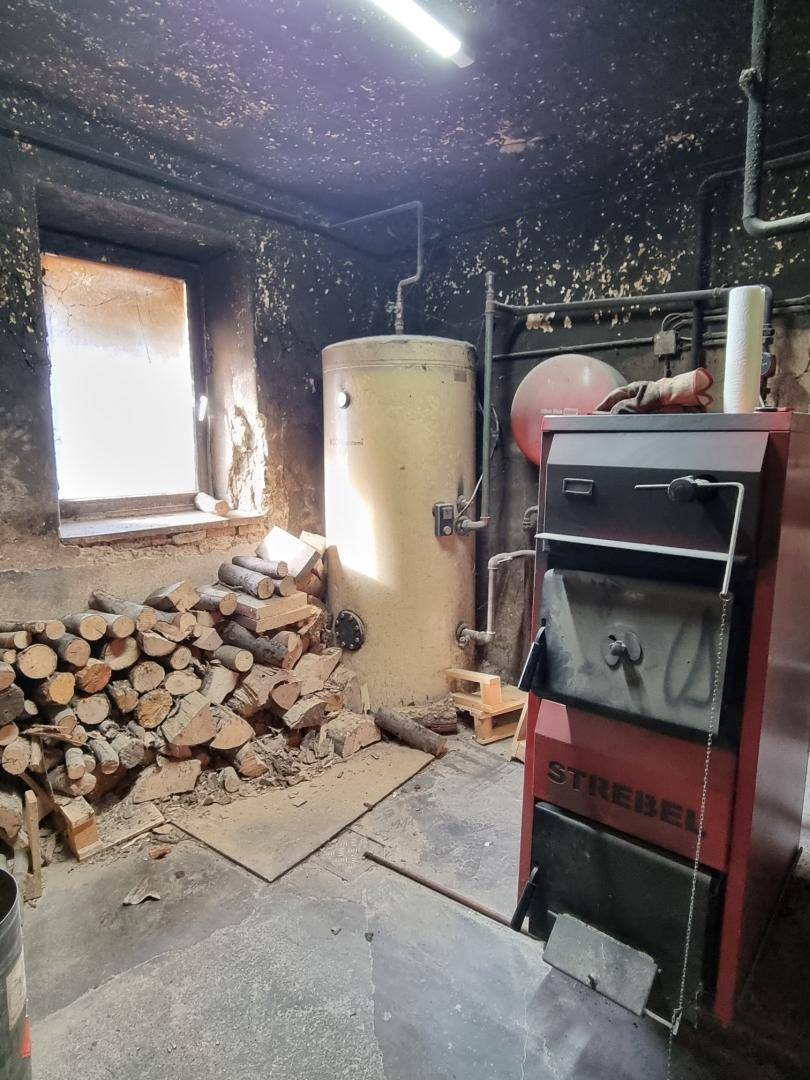 Heizraum im Keller mit Holzscheiten, Boiler und altem Ofen.