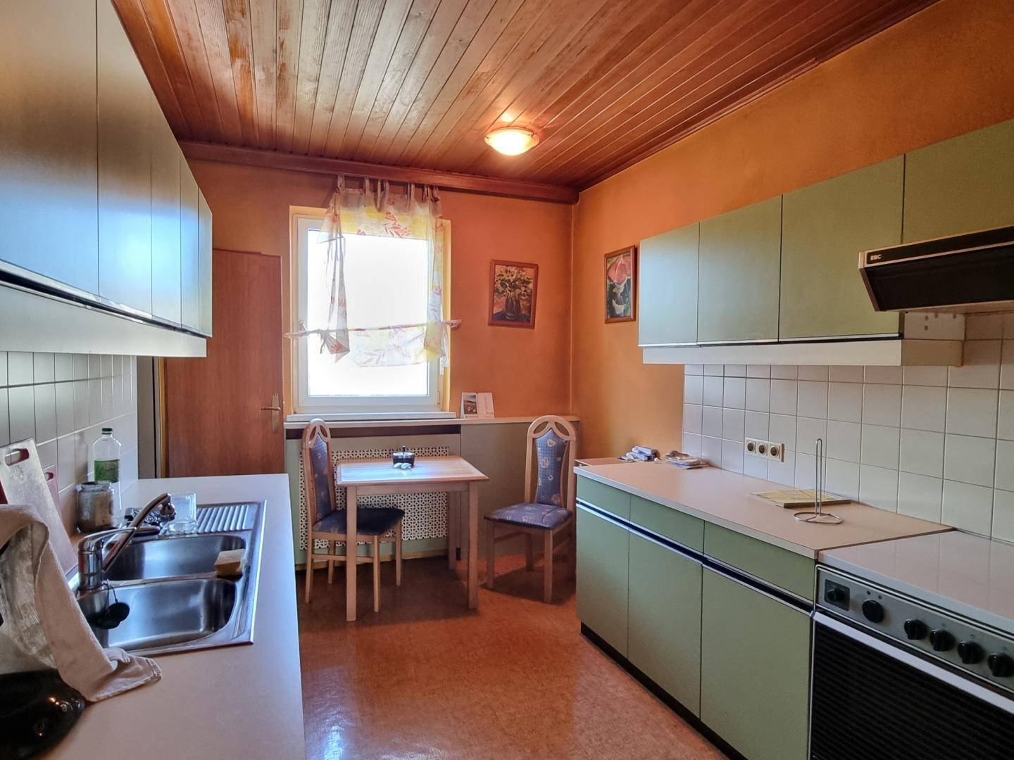 Traditionelle Küche mit Holzdecke, grünen Schränken, Essbereich und Fenster.